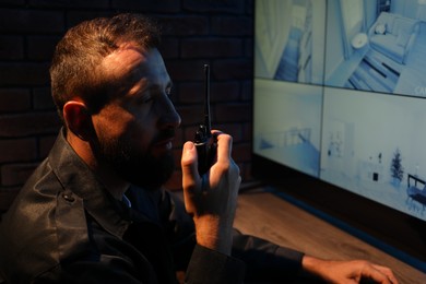 Photo of Security guard monitoring CCTV cameras and using walkie talkie in office at night
