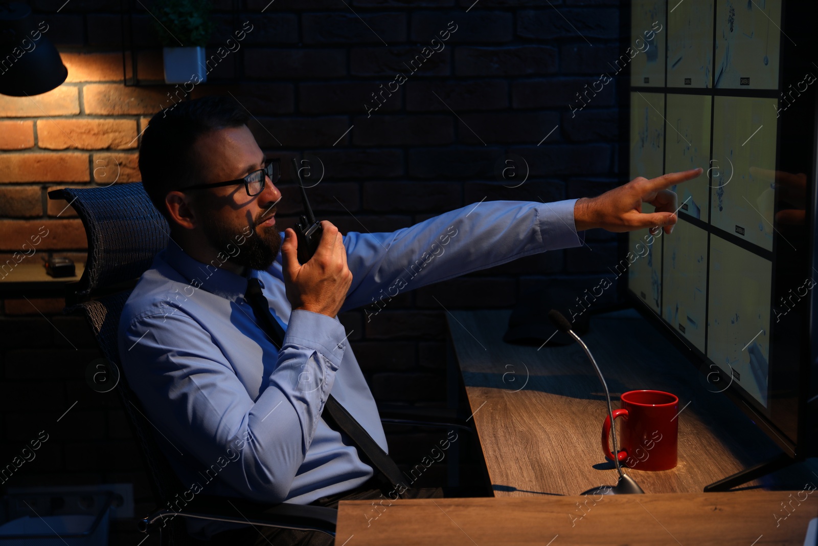 Security guard monitoring CCTV cameras and using walkie talkie in office at night Photo of Security guard monitoring CCTV cameras and using walkie talkie in office at night