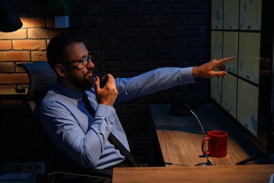 Photo of Security guard monitoring CCTV cameras and using walkie talkie in office at night