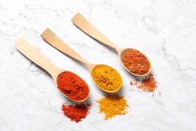 Photo of Different aromatic spices in wooden spoons on white marble table, flat lay