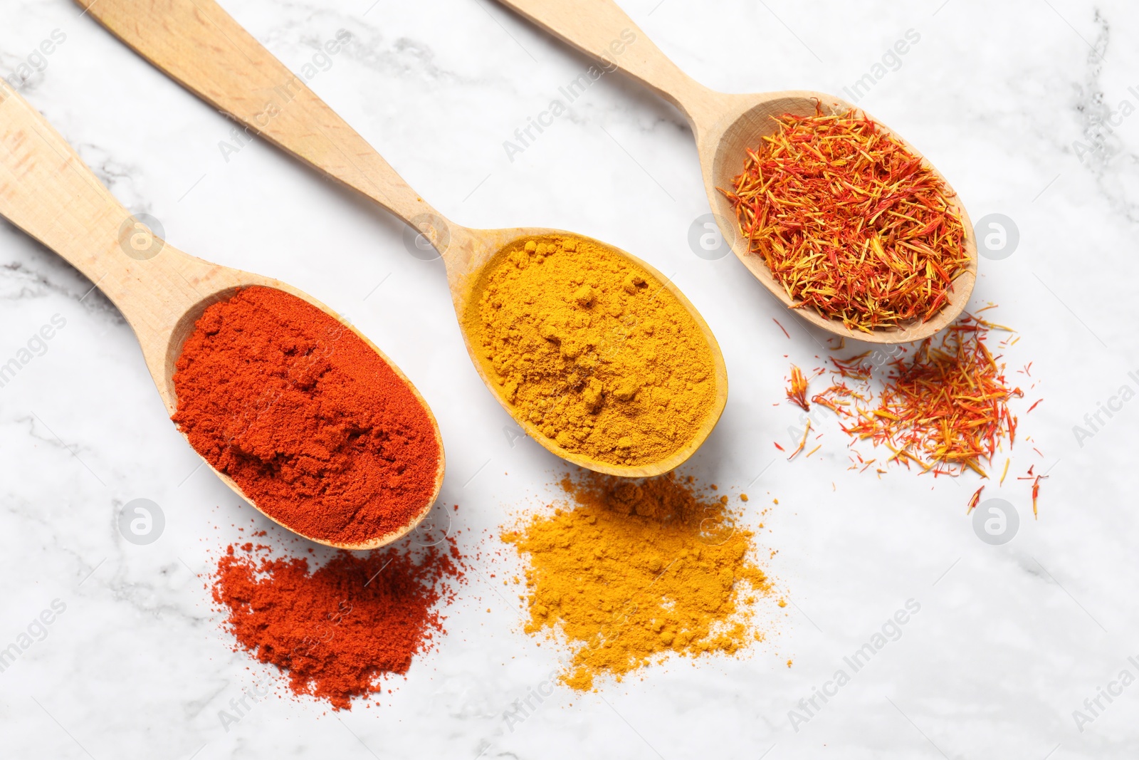 Photo of Different aromatic spices in wooden spoons on white marble table, flat lay
