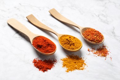 Photo of Different aromatic spices in wooden spoons on white marble table, closeup