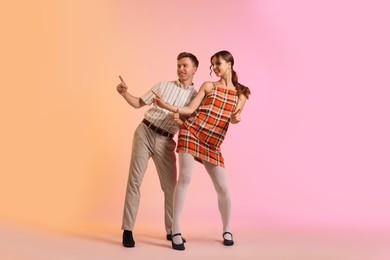 Photo of Happy couple in retro outfits dancing on color background