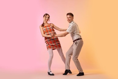 Photo of Happy couple in retro outfits dancing on color background