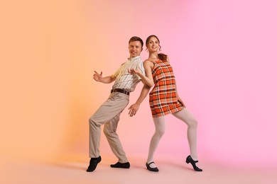 Photo of Happy couple in retro outfits dancing on color background