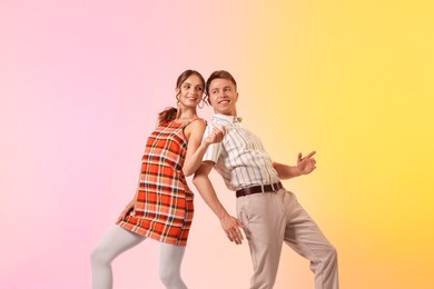 Photo of Happy couple in retro outfits dancing on color background