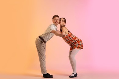 Photo of Happy couple in retro outfits dancing on color background
