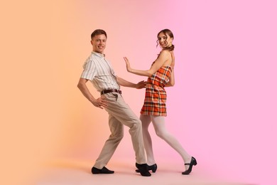 Photo of Happy couple in retro outfits dancing on color background