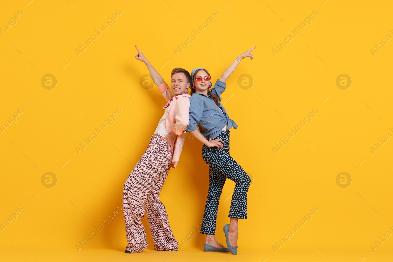 Happy couple in retro outfits dancing on orange background Photo of Happy couple in retro outfits dancing on orange background