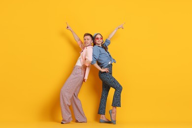 Photo of Happy couple in retro outfits dancing on orange background