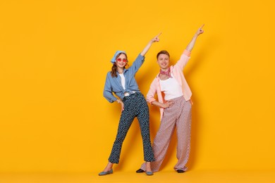 Photo of Happy couple in retro outfits dancing on orange background