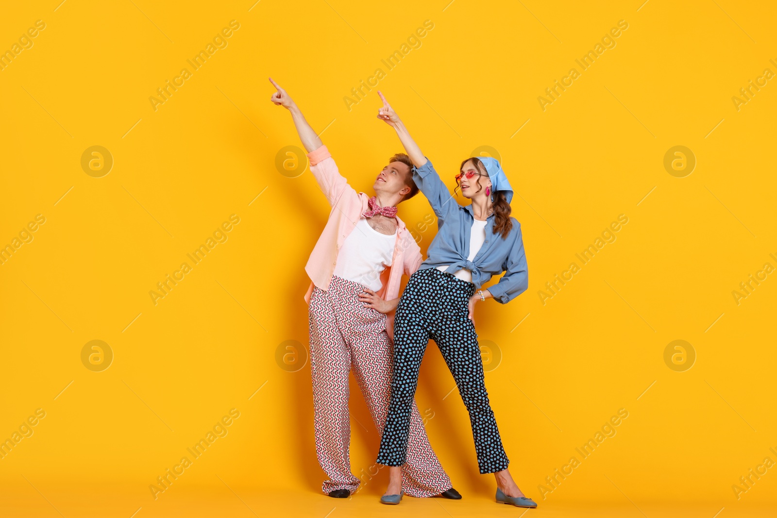 Photo of Happy couple in retro outfits dancing on orange background