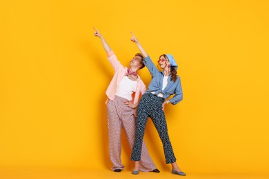 Photo of Happy couple in retro outfits dancing on orange background