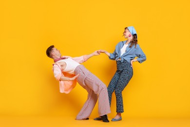 Photo of Happy couple in retro outfits dancing on orange background