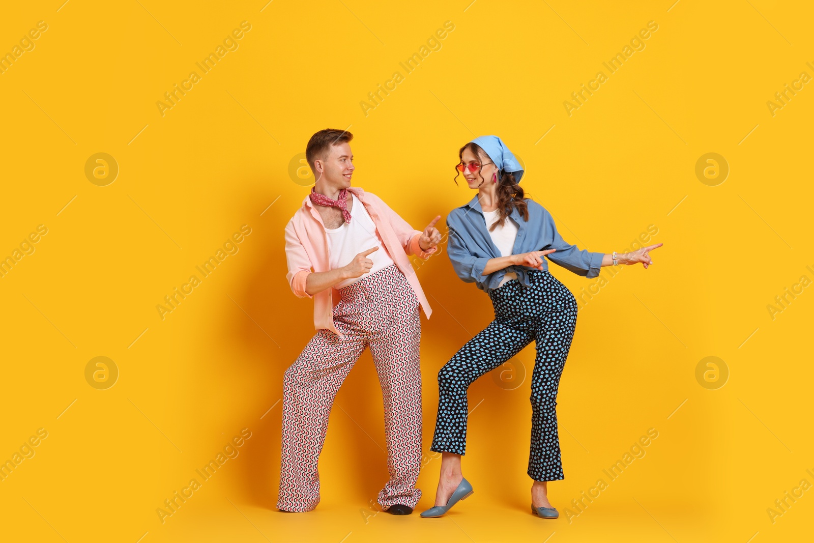Photo of Happy couple in retro outfits dancing on orange background