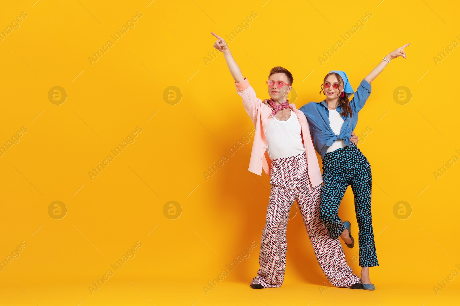 Photo of Happy couple in retro outfits dancing on orange background, space for text
