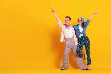 Photo of Happy couple in retro outfits dancing on orange background, space for text
