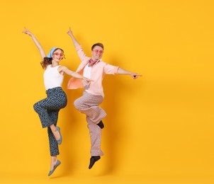 Photo of Happy couple in retro outfits dancing on orange background, space for text