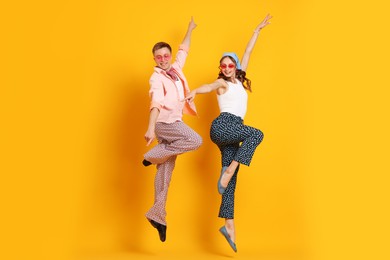 Photo of Happy couple in retro outfits dancing on orange background