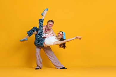 Photo of Happy couple in retro outfits dancing on orange background, space for text