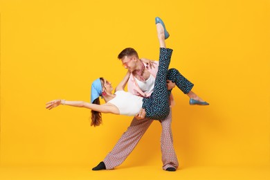 Photo of Happy couple in retro outfits dancing on orange background