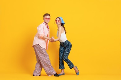 Photo of Happy couple in retro outfits dancing on orange background, space for text