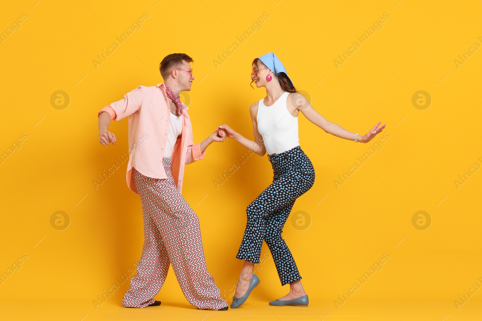 Photo of Happy couple in retro outfits dancing on orange background