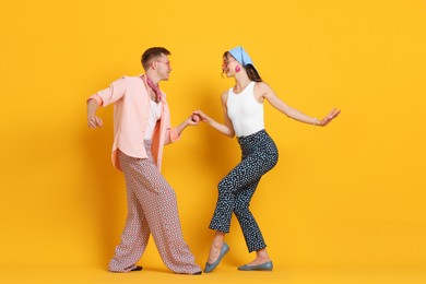 Photo of Happy couple in retro outfits dancing on orange background