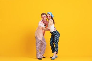 Photo of Happy couple in retro outfits dancing on orange background