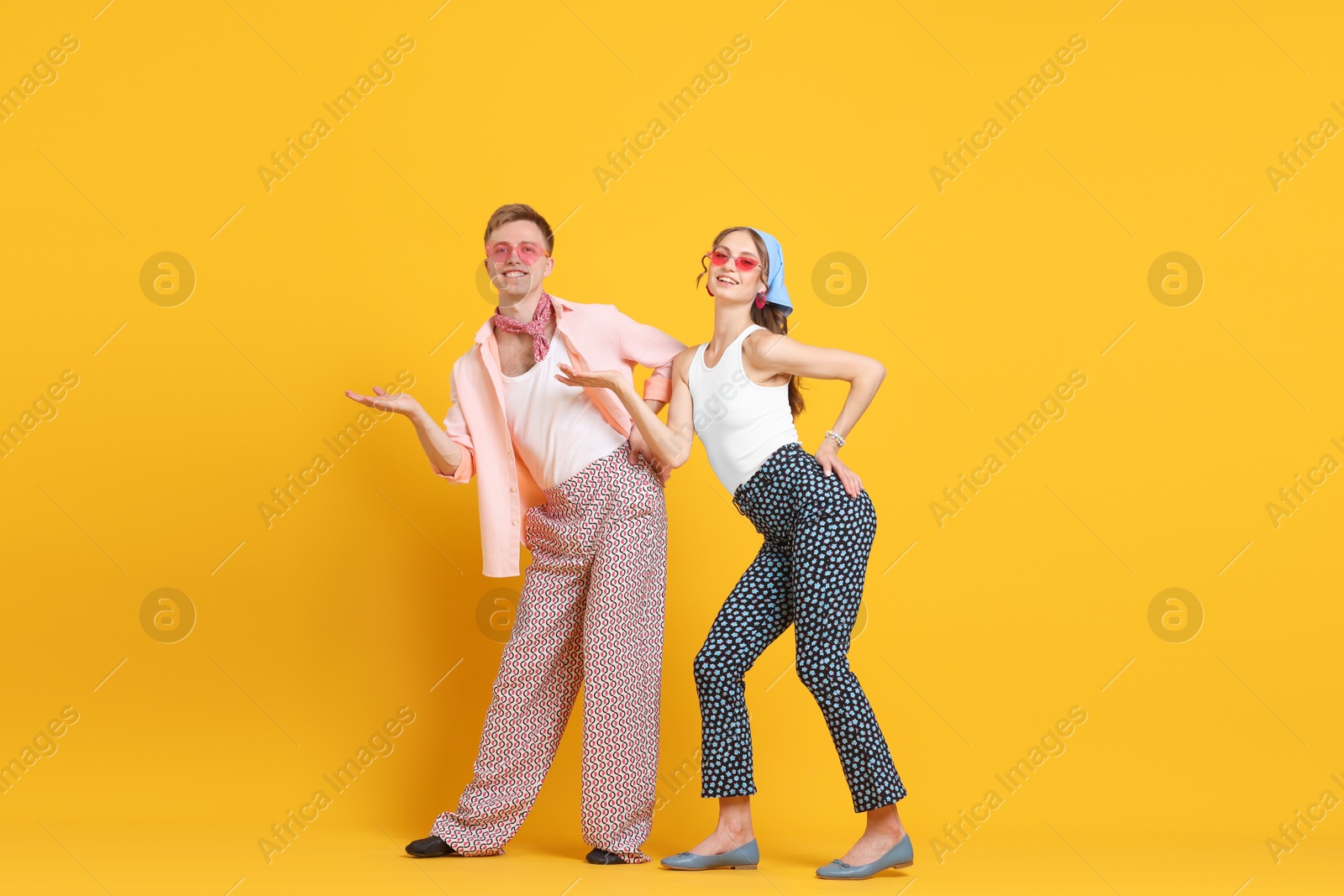Photo of Happy couple in retro outfits dancing on orange background