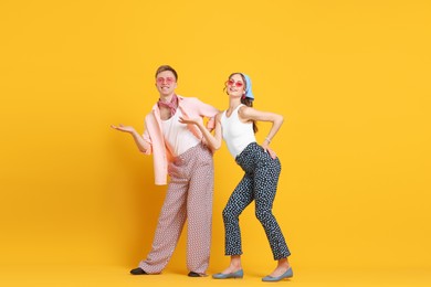 Photo of Happy couple in retro outfits dancing on orange background