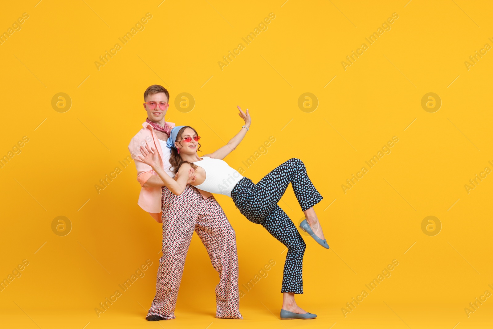 Photo of Happy couple in retro outfits dancing on orange background, space for text
