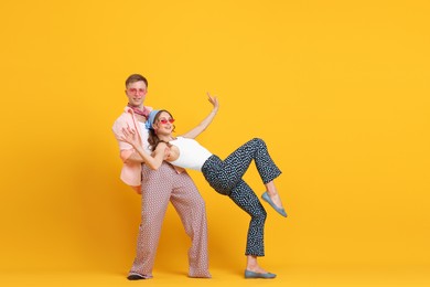Photo of Happy couple in retro outfits dancing on orange background, space for text