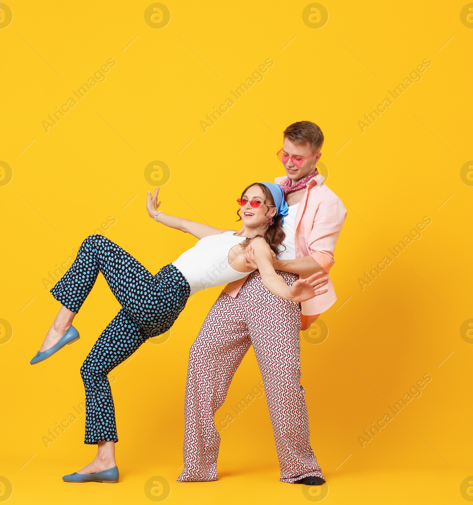 Photo of Happy couple in retro outfits dancing on orange background