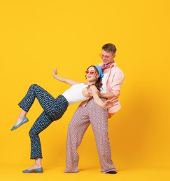 Photo of Happy couple in retro outfits dancing on orange background