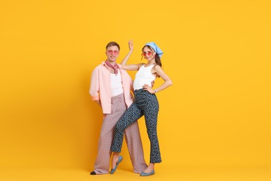 Photo of Happy couple in retro outfits dancing on orange background, space for text