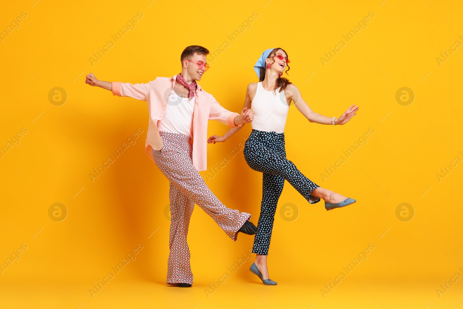 Happy couple in retro outfits dancing on orange background Photo of Happy couple in retro outfits dancing on orange background
