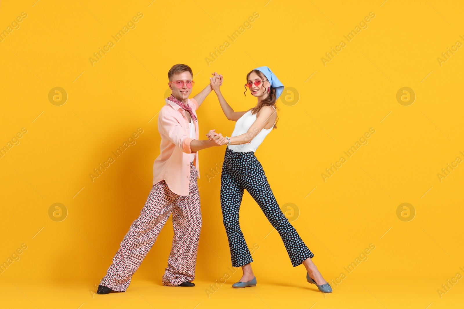 Happy couple in retro outfits dancing on orange background Photo of Happy couple in retro outfits dancing on orange background