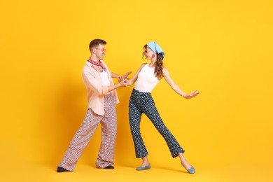 Photo of Happy couple in retro outfits dancing on orange background