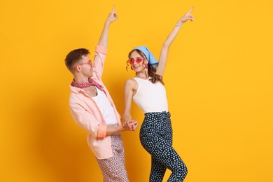 Photo of Happy couple in retro outfits dancing on orange background