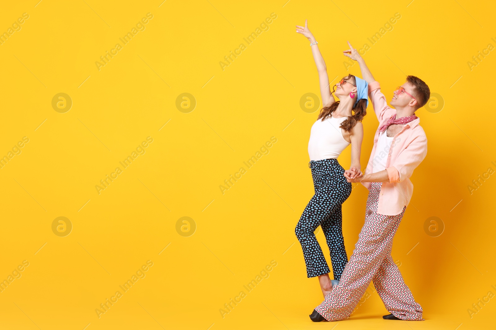 Happy couple in retro outfits dancing on orange background, space for text Photo of Happy couple in retro outfits dancing on orange background, space for text