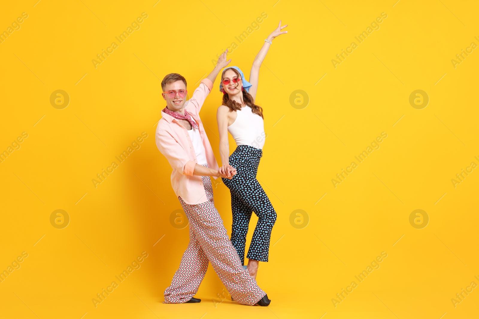 Happy couple in retro outfits dancing on orange background, space for text Photo of Happy couple in retro outfits dancing on orange background, space for text
