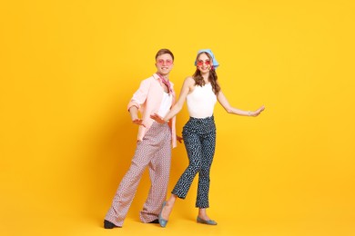 Photo of Happy couple in retro outfits dancing on orange background
