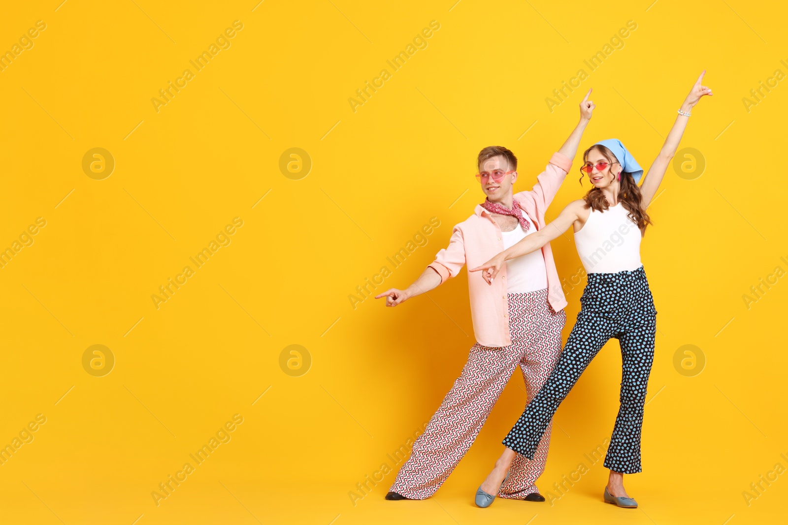 Photo of Happy couple in retro outfits dancing on orange background, space for text