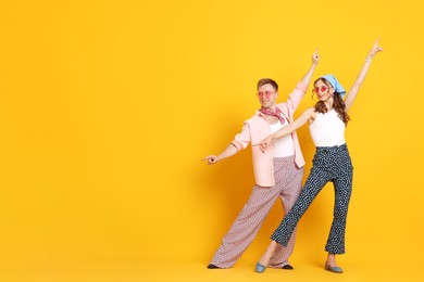 Photo of Happy couple in retro outfits dancing on orange background, space for text