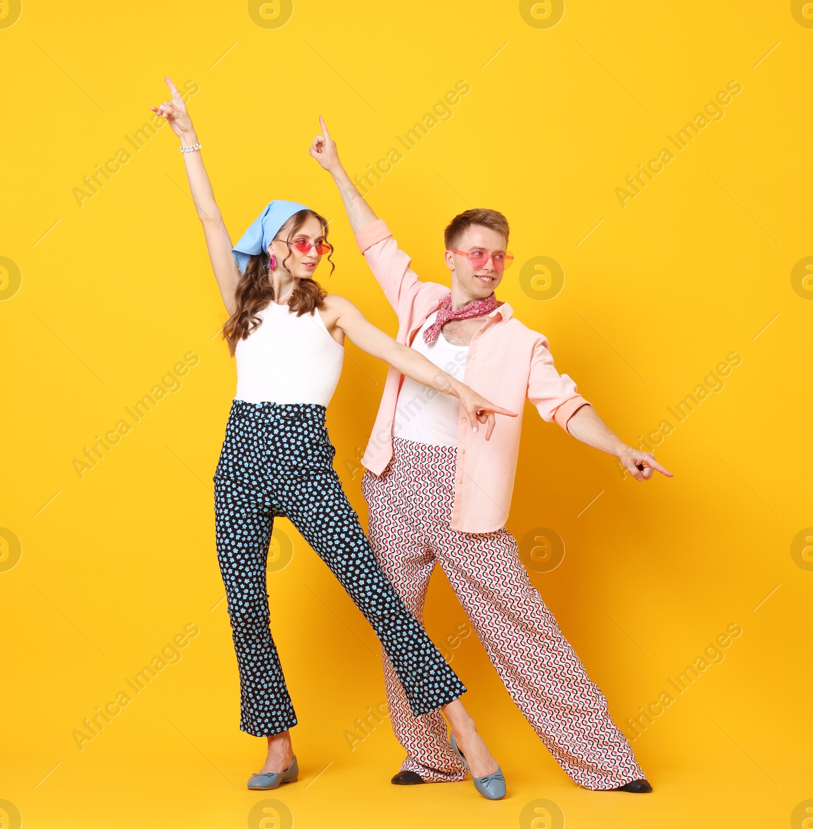 Photo of Happy couple in retro outfits dancing on orange background