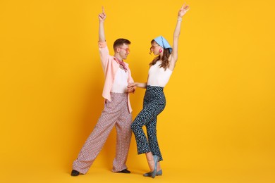 Photo of Happy couple in retro outfits dancing on orange background