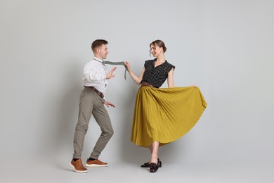 Photo of Happy couple in retro outfits dancing on light grey background