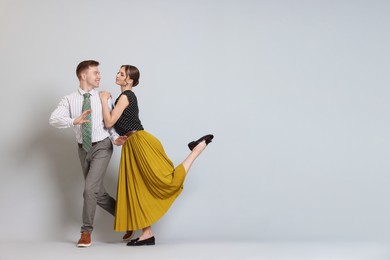 Photo of Happy couple in retro outfits dancing on light grey background, space for text
