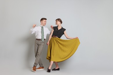 Photo of Happy couple in retro outfits dancing on light grey background, space for text